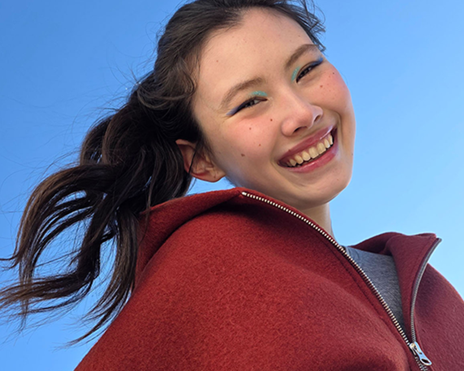 Young woman smiling with a blue sky in the background, showcasing the ability to capture selfies in a portrait style.
